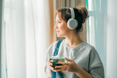 Genç bir kadın müzik dinler, kahve ya da çay içer ve pencereden dışarı bakar. Sakin bir kadın evde boş vakit geçirir. Kablosuz kulaklıklı favori şarkının tadını çıkar. Hafta sonu eğlencesi rahatla, stres yok.