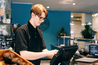 Genç garson, kafede müşteriye servis yapıyor. POS terminalinde çalışan bir adam. Kasiyer, kahveci ödeme makbuzunu kontrol ediyor. Konukseverlik, sunucu ve kahve dükkanında fişi hazırlama.