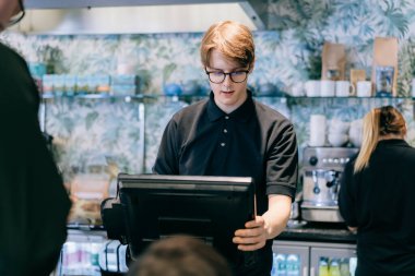 Genç garson, kafede müşteriye servis yapıyor. POS terminalinde çalışan bir adam. Kasiyer, kahveci ödeme makbuzunu kontrol ediyor. Konukseverlik, sunucu ve kahve dükkanında fişi hazırlama