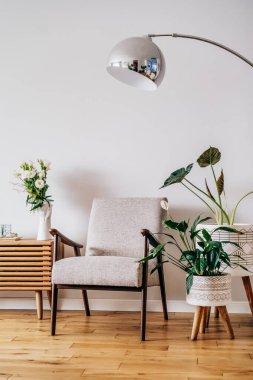 Modern İskandinav tarzı oturma odasının içinde mumlar, ahşap konsol, retro tarzı koltuk, yer lambası ve saksı yeşili ev bitkileri var. Konforlu ev iç tasarımı. Dikey