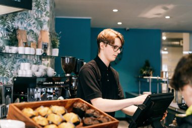 Genç garson, kafede müşteriye servis yapıyor. POS terminalinde çalışan bir adam. Kasiyer, kahveci ödeme makbuzunu kontrol ediyor. Konukseverlik, sunucu ve kahve dükkanında fişi hazırlama