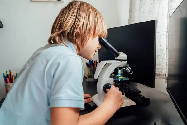 Caucasian boy using a microscope at home at his study place. Child curiosity, thirst for knowledge, home learning experience, home remote education concepts. Selective focus