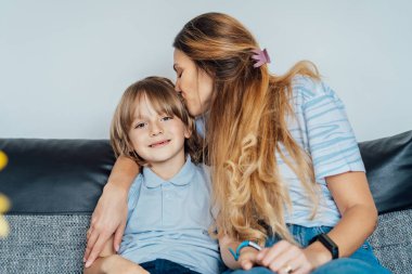 Evde gülümseyen mutlu bir ailenin portresi. Oğlu ve annesi kanepede oturuyor, birbirlerine sarılıyorlar, anne oğlunu öpüyor hafta sonu aile tatilinde. Seçici odak