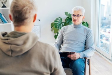 Profesyonel psikoterapi. Ruh sağlığı kliniğinde erkek hastayla seans yapan erkek psikolog ofisinde randevu sırasında not alıyor. Psikolojik yardım servisi. Depresyon tedavisi.