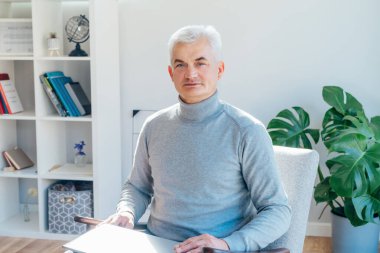 Profesyonel psikoterapi çevrimiçi. Orta yaşlı erkek psikolog koltukta otururken dizüstü bilgisayarında video görüşmesi yapıyor. Uzman konuşması, danışmanlık, hastaya online yardım.