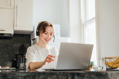 Uzaktan kumandalı iş. Mutfak Masası 'nda dizüstü bilgisayarda çalışan kulaklıklı duygusal kadın. Öğrencinin çevrimiçi dersleri var. Müdürün video toplantısı var. Tele pazarlama servisinde müşteri destek operatörü.