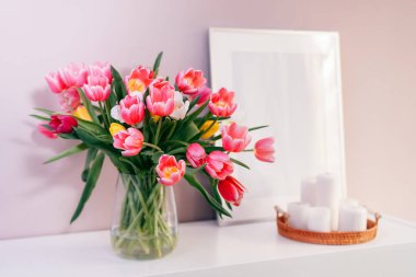 Vazodaki lale çiçeği buketine odaklı modern iç tasarım, beyaz çerçeve modeli, pembe arka plandaki beyaz konsoldaki mumlar. Poster tasarımı modeli. Minimalist Ev Dekorasyonu