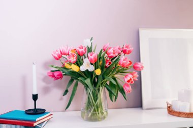 İçinde lale çiçekleri olan modern iç tasarım vazo, beyaz resim çerçeve modeli, pembe duvar zemininde beyaz konsoldaki mumlar. Poster tasarımı modeli. Minimalist ev dekorasyonu. Seçici odak.