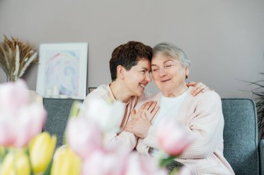 Yetişkin bir kadın sevinçle sarılıyor, kıdemli anne bulanık lalelerle güzel bir anı paylaşıyor. Ebeveyn sevgisi, özen ve birlik kavramı. Anneler Günü. Mutlu aile hafta sonu birlikte eğleniyor.