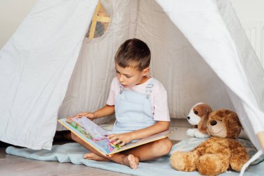 Sevimli küçük anaokulu çocuğu oyuncaklarına kitap okuyor rahat çocuklar çadırında oturuyor evdeki oturma odasında. Çocuk kendini eğlendiriyor. Ev çocukları etkinliği