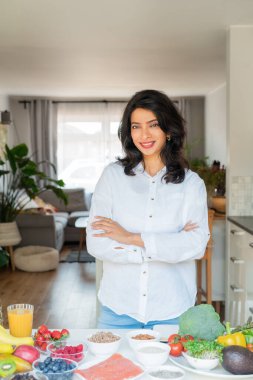 Kendinden emin orta yaşlı Hintli kadın beslenme uzmanı kollar mutfak masasının önünde meyve ve sebze dolu. Sağlıklı beslenme alışkanlıkları ve sağlık yaşam tarzı, kilo verme programı