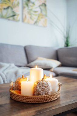Hygge ev dekoru için sonbahar havası kompozisyonu. Mandalalarla süslenmiş turuncu balkabakları oturma odasındaki sehpada hasır tepside mum yakıyorlar. Seçici odaklanma. Boşluğu kopyala