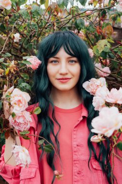 Gülümseyen romantik hippi kadının portresi. Yeşil saçlı, pembe mor elbiseli ve çiçek açan arka planda ceketli. Sokak modası. Gen Z. Yaz tatili, eğlence, pozitif ruh hali. Dikey.