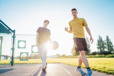 Gün batımında parkın bahçesinde basketbol oynayan iki genç beyaz erkek. Gençlerin hobisi, çevrimdışı aktiviteler. Spor anlayışı, hobiler ve sağlıklı yaşam tarzı. Seçici odak