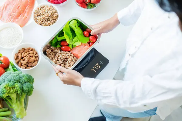 stock image Healthy diet plan for weight loss, daily ready meal menu. Close up Woman weighing lunch box cooked in advance,ready to eat on kitchen scale. Balanced portion with healthy dish. Pre-cooking concept.
