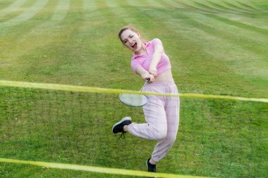 Şehir parkında raketle badminton oynayan bağıran genç bir kadın. Arkadaşlar dışarıda eğleniyor. Oyunun ve doğal çevrenin tadını çıkarıyorum. Yetişkin açık hava aktivitesi. Sağlıklı yaşam tarzı