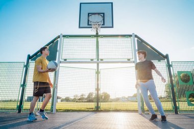 Gün batımında parkın bahçesinde basketbol oynayan iki genç beyaz erkek. Gençlerin hobisi, çevrimdışı aktiviteler. Spor anlayışı, hobiler ve sağlıklı yaşam tarzı. Seçici odak
