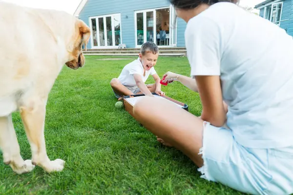 stock image Joyful little boy and his mother are playing portable air hockey in the garden. Fun Playing Games in Backyard Lawn on Summer Day. Happy family time with pet together. Solo parenting. Active childhood