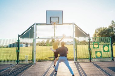 Gün batımında parkın bahçesinde basketbol oynayan iki genç beyaz erkek. Gençlerin hobisi, çevrimdışı aktiviteler. Spor anlayışı, hobiler ve sağlıklı yaşam tarzı. Seçici odak