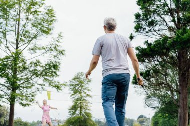 Parkta genç bir kadınla raketle badminton oynamaya odaklan. Arkadaşlar dışarıda eğleniyor ve antrenman yapıyor. Oyunun ve doğal çevrenin tadını çıkarıyorum. Yetişkin açık hava aktivitesi. Sağlıklı yaşam tarzı.