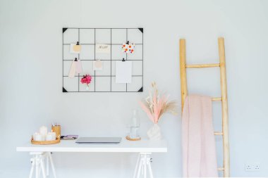 Ev ofis iş yeri tasarımı. Açık dizüstü bilgisayarı olan beyaz masa şeftali ve pembe renk paletli ızgara ruh hali tahtası ve mumlar gibi kadınsı dekorlar, kurumuş çiçekler. İlham ve ruh hali konsepti