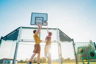 Gün batımında parkın bahçesinde basketbol oynayan iki genç beyaz erkek. Gençlerin hobisi, çevrimdışı aktiviteler. Spor anlayışı, hobiler ve sağlıklı yaşam tarzı. Seçici odak