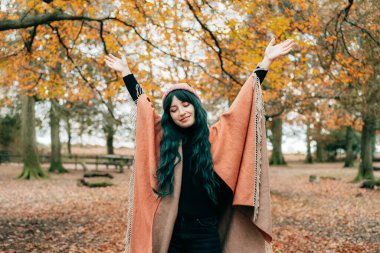 Sıcak şala sarılmış, şapkalı gülümseyen kadın sarı yapraklarla sonbahar ormanında hayatın ve özgürlüğün tadını çıkaran Panço kollarını kaldırdı. Ahengi hissetmek, doğayla bir araya gelmek. Rahatlatıcı, kişisel tatmin.