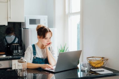 Uzaktan kumandalı iş. Mutfak Masası 'ndaki küçük dairelerde dizüstü bilgisayarda çalışan konsantre genç bir kadın. İnternetten ders alan bir kız öğrenci, evden çalışan bir serbest çalışan. Çevrimiçi Görev