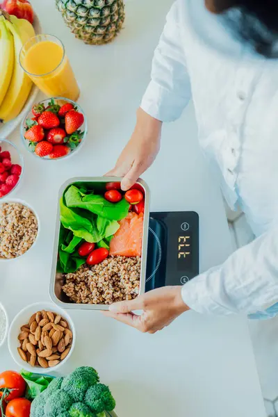 stock image Healthy diet plan for weight loss, daily ready meal menu. Close up Woman weighing lunch box cooked in advance,ready to eat on kitchen scale. Balanced portion with healthy dish. Pre-cooking concept.