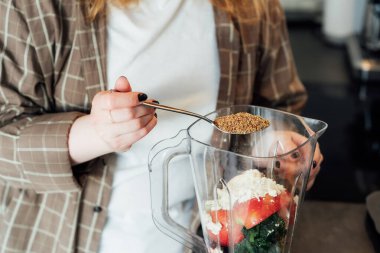 Close up woman adding flex seeds during making smoothie on the kitchen. Superfood supplement. Healthy detox vegan diet. Healthy dieting eating, weight loss program. Selective focus. Copy space clipart