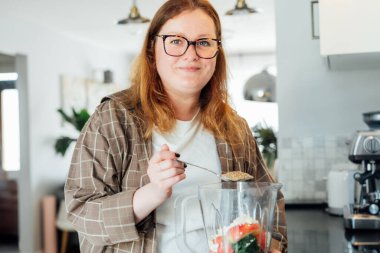 Artı, mutfakta meyve püresi yaparken esnek tohum ekleyen boyda bir kadın. Süper gıda takviyesi. Sağlıklı detoks vegan diyeti. Sağlıklı beslenme, kilo verme programı. Seçici odak