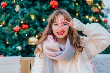 Süslü bir Noel ağacında baston şekerlerle yapılmış kalp şeklinde gülümseyen genç bir kadın. Mutlu yıllar Noel tatilleri. Aşkı ve hayırseverlik konseptini paylaşma zamanı.