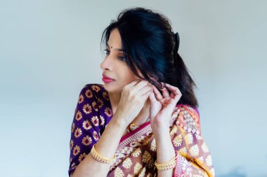 Güzel bir sari giymiş, Hintli bir kadın geleneksel mücevherleri kibarca koyuyor ve etnik bir kutlama için hazırlanıyor. Modern hayatta Hint kültürü ve dini bayramlar. Seçici odak.