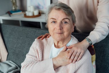 Gülümseyen yaşlı bir kadın genç akrabalarını hissediyor ya da omzunda bakıcı destekleyici bir dokunuş. Yaşlı ebeveynler, büyükanne ve büyükbabalar bakım ve destek. Aile nesli ilişkileri kavramı. Yaş bakımı