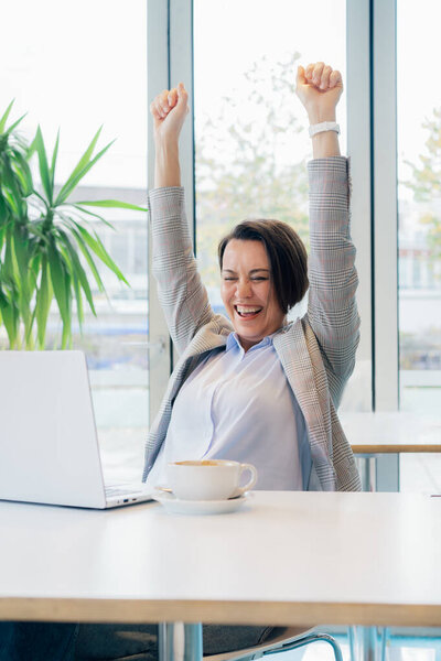 Excited happy middle aged business woman with laptop feeling winner rejoicing online win got new job opportunity, overjoyed motivated lady doing yes gesture, receive good result, celebrating in office