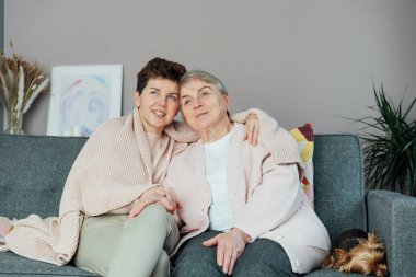 Tarafsız bir cinsiyet kadını, kıdemli annesine ya da büyükannesine sarılıyor ve televizyon seyrediyor, birlikte hassas anlarını paylaşıyor. Ebeveyn sevgisi, bakım ve nesiller boyu birlik kavramı. Anneler Günü. Mutlu aile hafta sonu eğleniyor