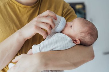 Bebeğini karnında taşıyan ve mama şişesiyle besleyen bir baba. Yemek Evlat Edinme. Çocuk sağlığı ve cilt bakımı kavramı. Emzirme, gıda alerjisi, gazlı mide, kolik sorunları.