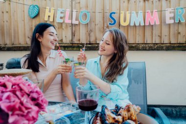 İki kadın kokteyl içiyor, yaz tatilinin tadını çıkarıyor açık terasta içki ve atıştırmalıklarla birlikte. Arkadaşlar yemek yiyor, veranda partisinde birlikte eğleniyorlar. Merhaba yaz konsepti