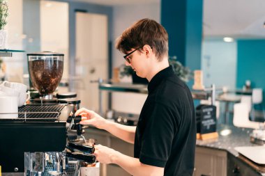 Genç barista modern bir kahve dükkanında otomatik makinede kahve yapıyor. Öğrenci kafede yarı zamanlı çalışıyor. İşsizlik sorunları ve gençler için iş olanakları. Küçük işletme boşlukları.