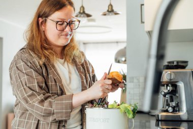 Mutfak atıklarını gübrelemek, evde geri dönüşüm yapmak. Sebzeleri kesilen artıkları çöpe atan kadın mutfak masasındaki gübre kutusu. Çevresel sorumluluk, ekoloji. Seçici odak.