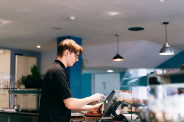 Genç garson, kafede müşteriye servis yapıyor. POS terminalinde çalışan bir adam. Yarı zamanlı çalışan bir öğrenci. İşsizlik sorunları ve gençler için iş olanakları. Küçük işletme boşlukları.