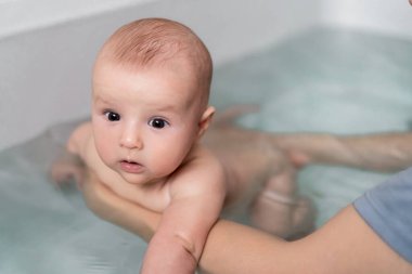 Güzel bebek banyoları ve banyoda yüzme. Bebek yüzmeyi ve spor yapmayı öğreniyor. Baba, meraklı bebeğiyle sıcak bir banyoda banyo yapmayı seviyor. Babalık kavramı. Seçici odak