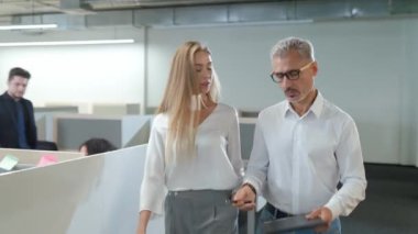 İdari ekip açık alanda çalışıyor, yönetici ve bayan meslektaşı ofiste dolaşıyor, iş arkadaşlarıyla ve uluslararası ekiple iletişim kuruyor..