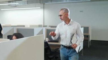 Uluslararası yönetim ekibi açık alanda çalışıyor, proje yöneticisi ofiste dolaşıyor ve iş arkadaşlarıyla iletişim kuruyor..