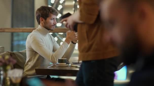 手持式 一个在笔记本电脑上工作的年轻自由职业者的肖像 专注的男人用智能手机 在咖啡馆里做远程工作 思考的过程 — 图库视频影像
