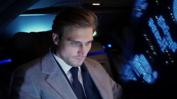 移動中の車に乗ってラップトップを使用している若いビジネスマンの肖像画 スーツの男の上のマネージャーはビジネス車の後ろに座っています 会議への夜乗り — ストック動画