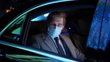 Ağır çekimde, tıbbi maskeli bir işadamı hareket halindeki bir arabada oturuyor ve dizüstü bilgisayar kullanıyor. Takım elbiseli üst düzey bir yönetici bir iş arabasının arkasında oturuyor..