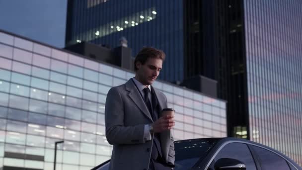 ビジネスカーの近くに立ち コーヒーを飲む陽気なビジネスマンの肖像画 スーツのトップマネージャー 背景にあるオフィスビル ハンドヘルド — ストック動画