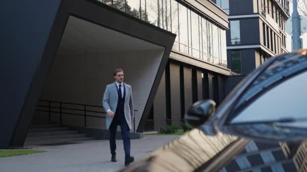 ビジネスマンは黒い車に歩き 会議のためのスーツの葉の優雅な男 バックグラウンドのオフィスの建物 4Kの遅い動きに座ります — ストック動画