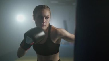 Kadın gücü, kadın boksör yumruklarını eğitiyor, kum torbasına vuruyor, boks salonunda antrenman günü, kadın hızlı saldırıyor, 4k ağır çekim..